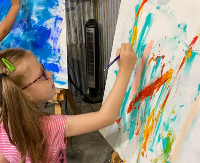 A Young Student Explores Color A student painting an acrylic painting at an easel with a brush.